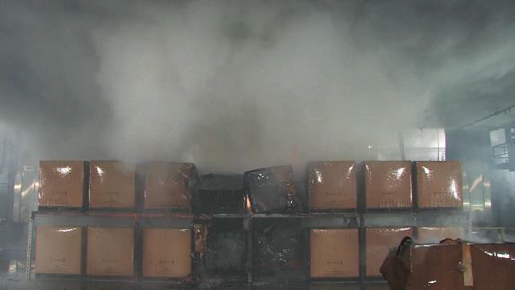 Fig. 2 – Fire test of automatic water mist nozzles over cardboard boxes conducted under the moveable ceiling in the Large Burn Laboratory at the FM Global Research Campus in Glocester, Rhode Island, USA. As the fire grows, it triggers multiple water mist nozzles. The fine droplets are sucked into the base of the fire and flash to steam, depriving the fire of essential oxygen. 